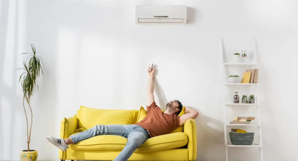 Férfi a kanapén fekve, távirányítóval kapcsolgatja a feje felett elhelyezett klímát